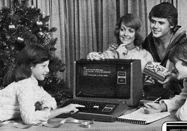 Uma criança usando um computador TRS-80 perto de uma árvore de Natal com os pais olhando.