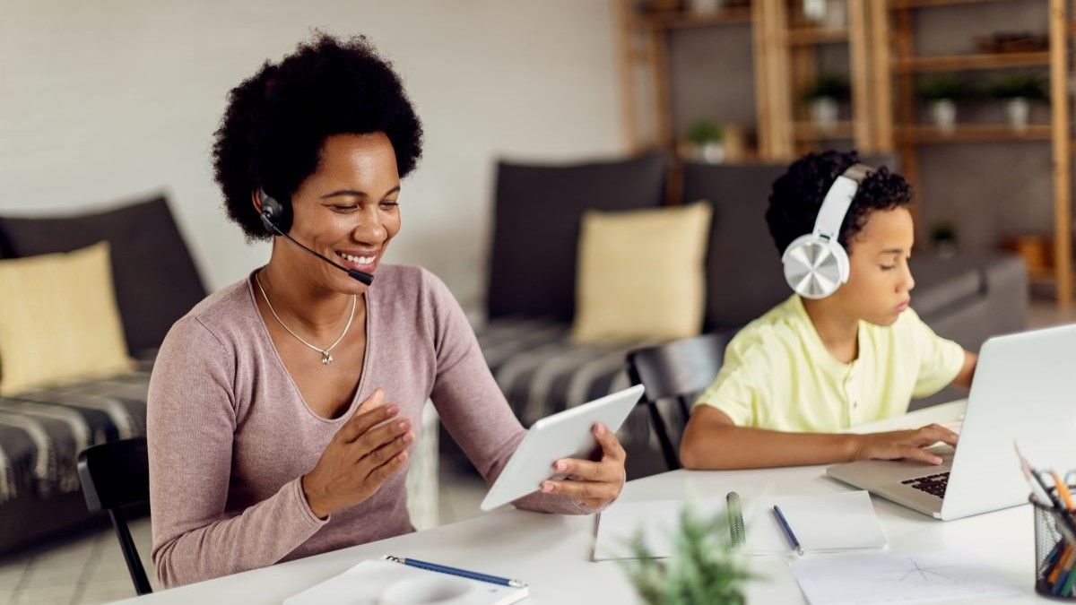 Uma mulher e uma criança usam fones de ouvido para conversar por voz em um tablet e laptop.