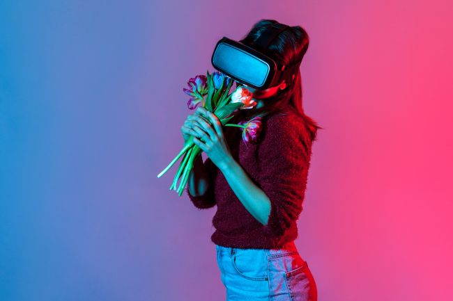 Mulher usando fone de ouvido de realidade virtual e apreciando o cheiro de um buquê de flores.