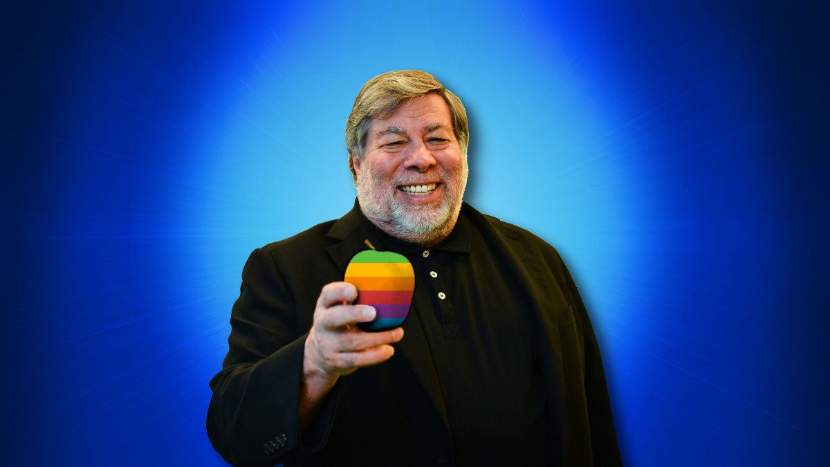 Steve Wozniak segurando uma maçã de seis cores sobre fundo azul em 2014