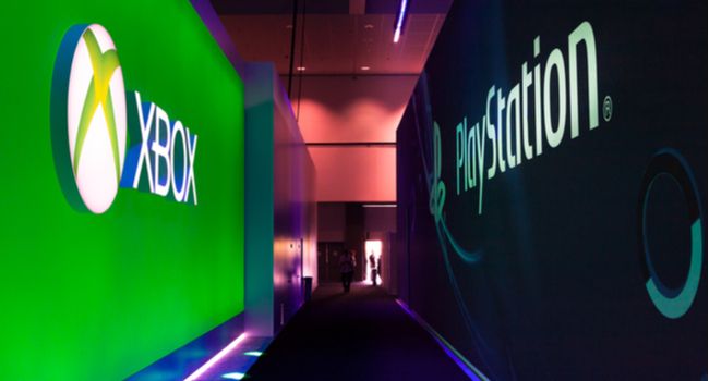 Corredor de uma conferência de jogos com o logotipo do Xbox de um lado e o logotipo do PlayStation do outro.
